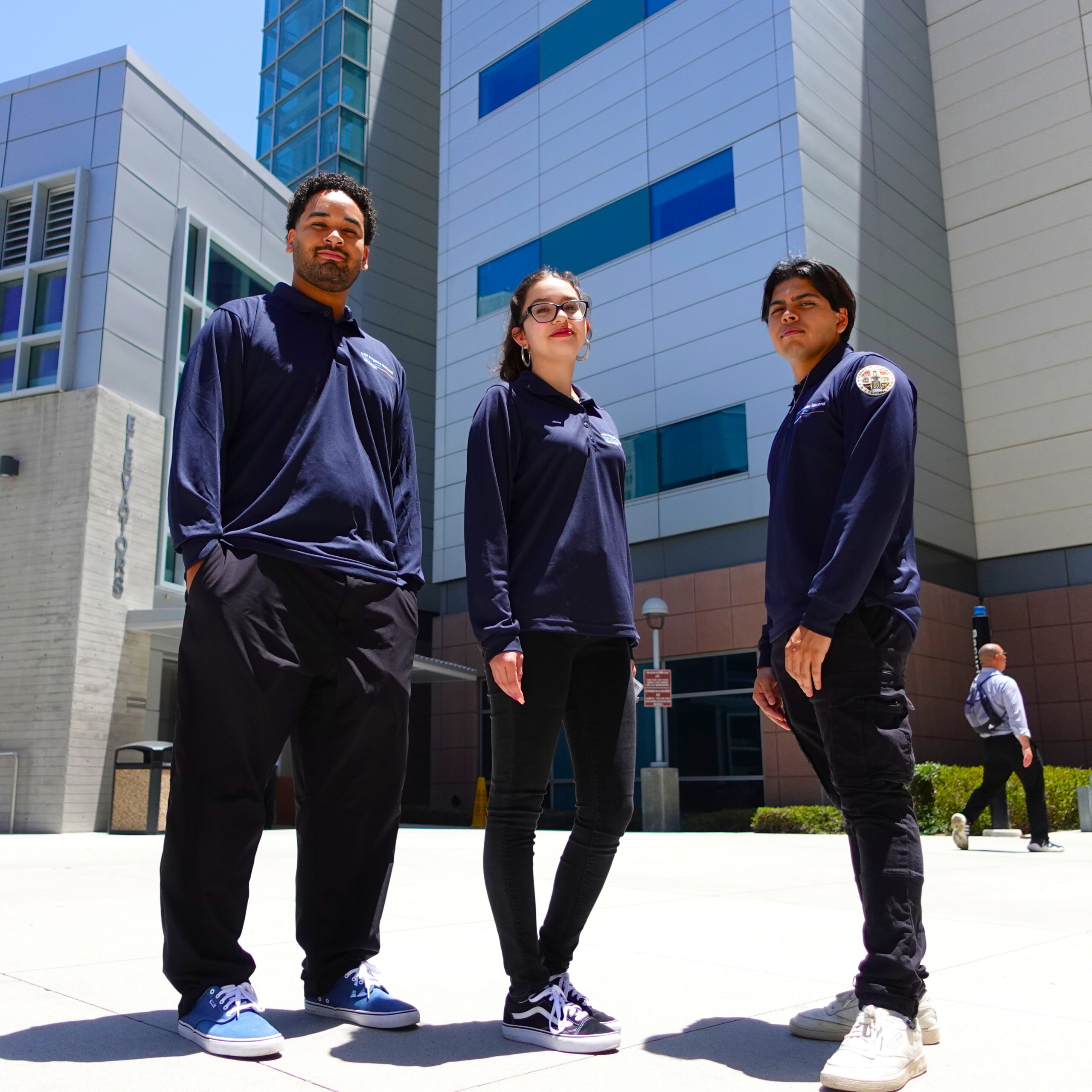 3 volunteers in navy blue Los Angeles General Medical Center Pull overs standing in front of Inpatient Tower