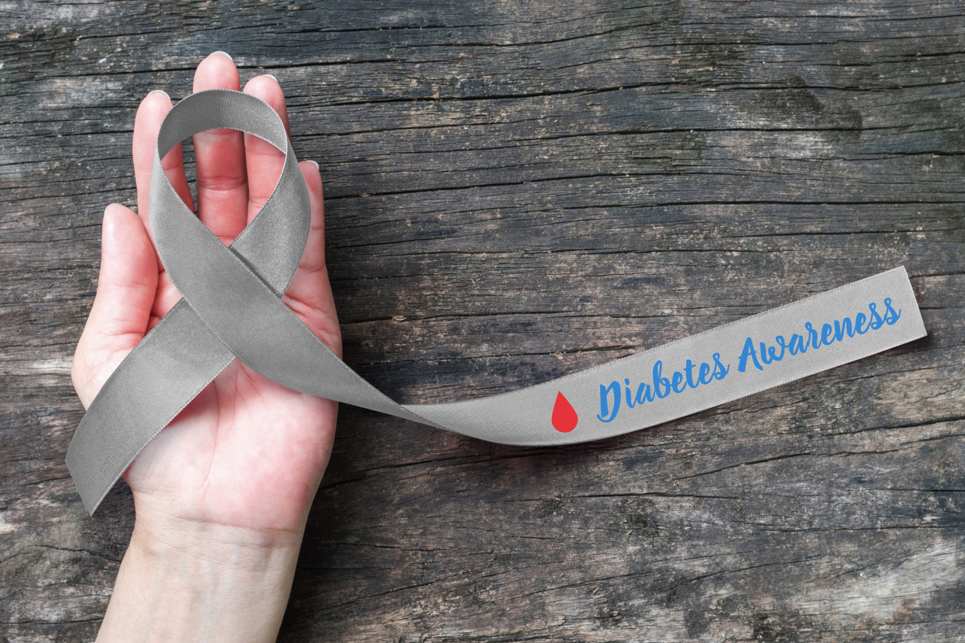 World diabetes day with grey and red blood drop ribbon for diabetic disease awareness, symbolic bow isolated with clipping path on helping hand support