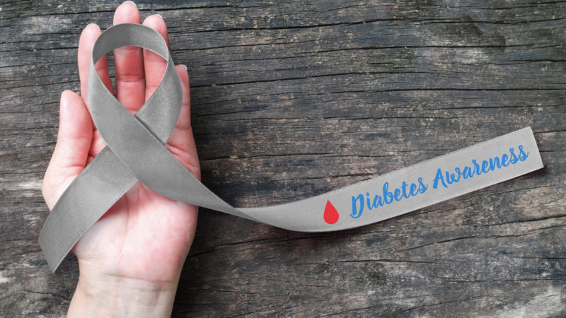World diabetes day with grey and red blood drop ribbon for diabetic disease awareness, symbolic bow isolated with clipping path on helping hand support