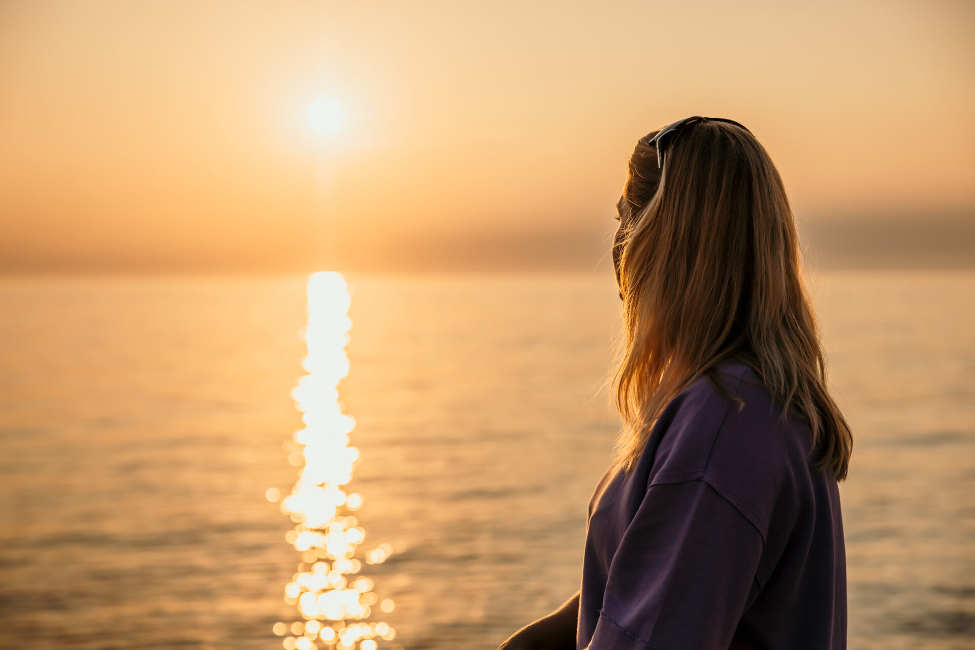 Adult woman with blonde hair enjoying the sunset at the sea with reflection on water surface